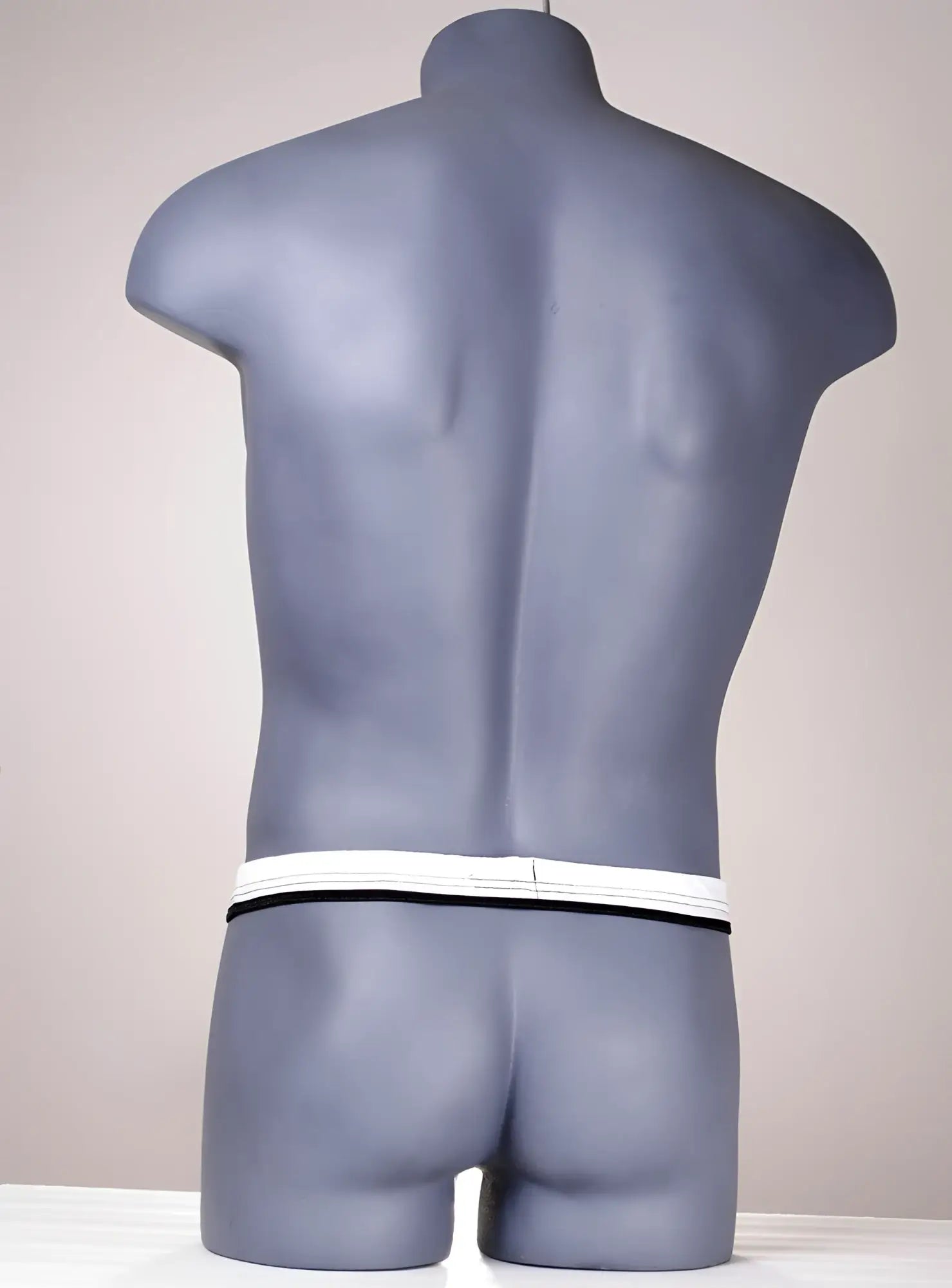 White and black thong on a grey male mannequin torso, showing the slim waistband from the back.