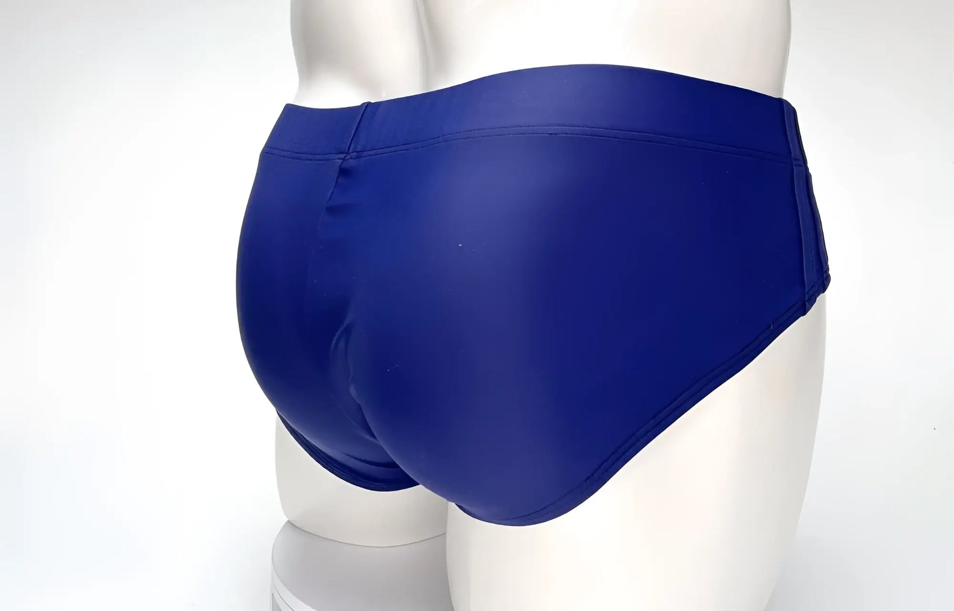 Back view of a WildmanT navy blue swim brief on a white mannequin torso, showing full coverage and side seams.