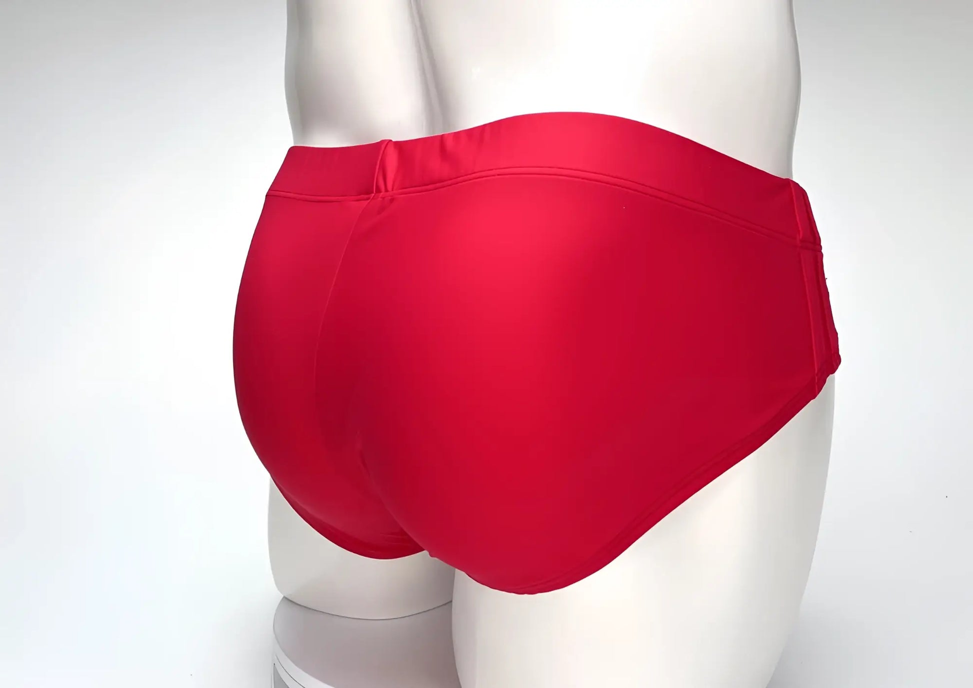 Back view of a solid red WildmanT Big Boy pouch swim brief on a white mannequin torso.