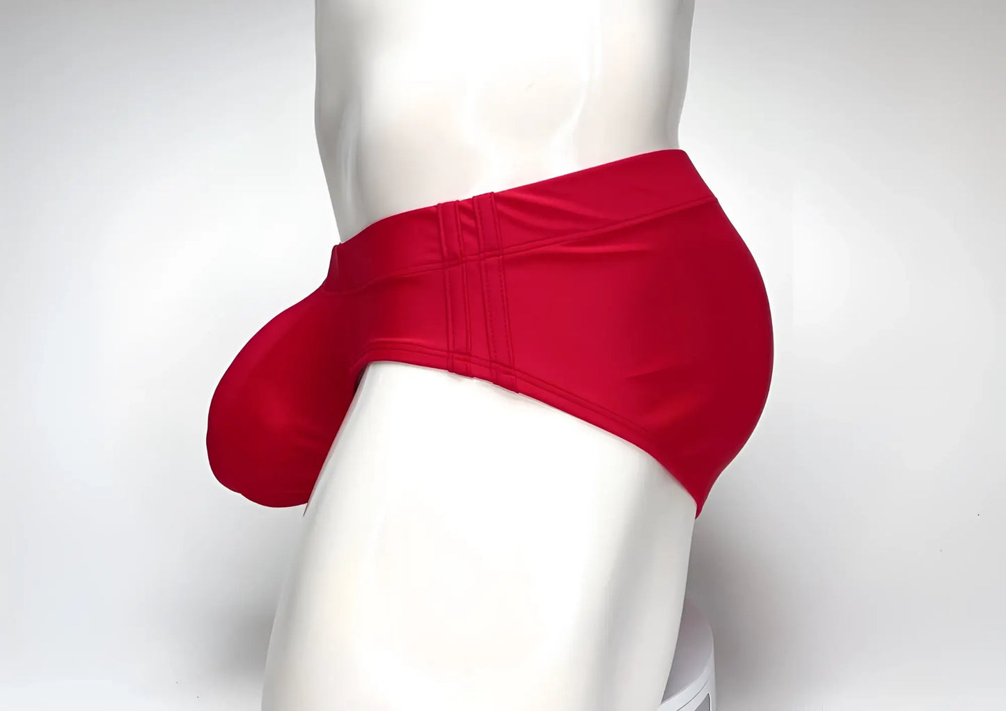 Bright red WildmanT swim brief with a prominent front pouch, shown from the side on a white mannequin torso.