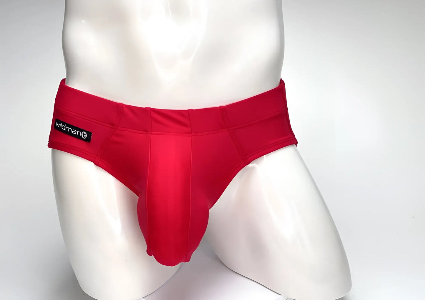 Bright red WildmanT swim brief with a prominent center pouch and black logo tag on a white mannequin torso.