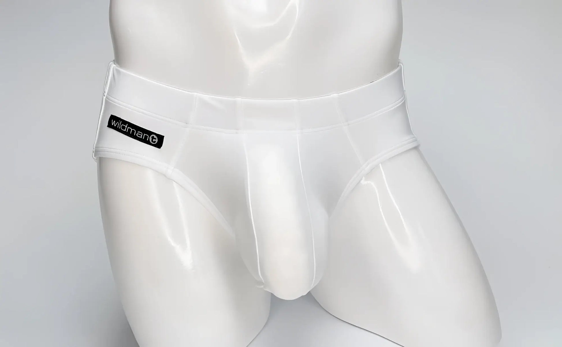 WildmanT white Big Boy pouch swim brief on a mannequin, featuring a black branded logo patch on the right hip.
