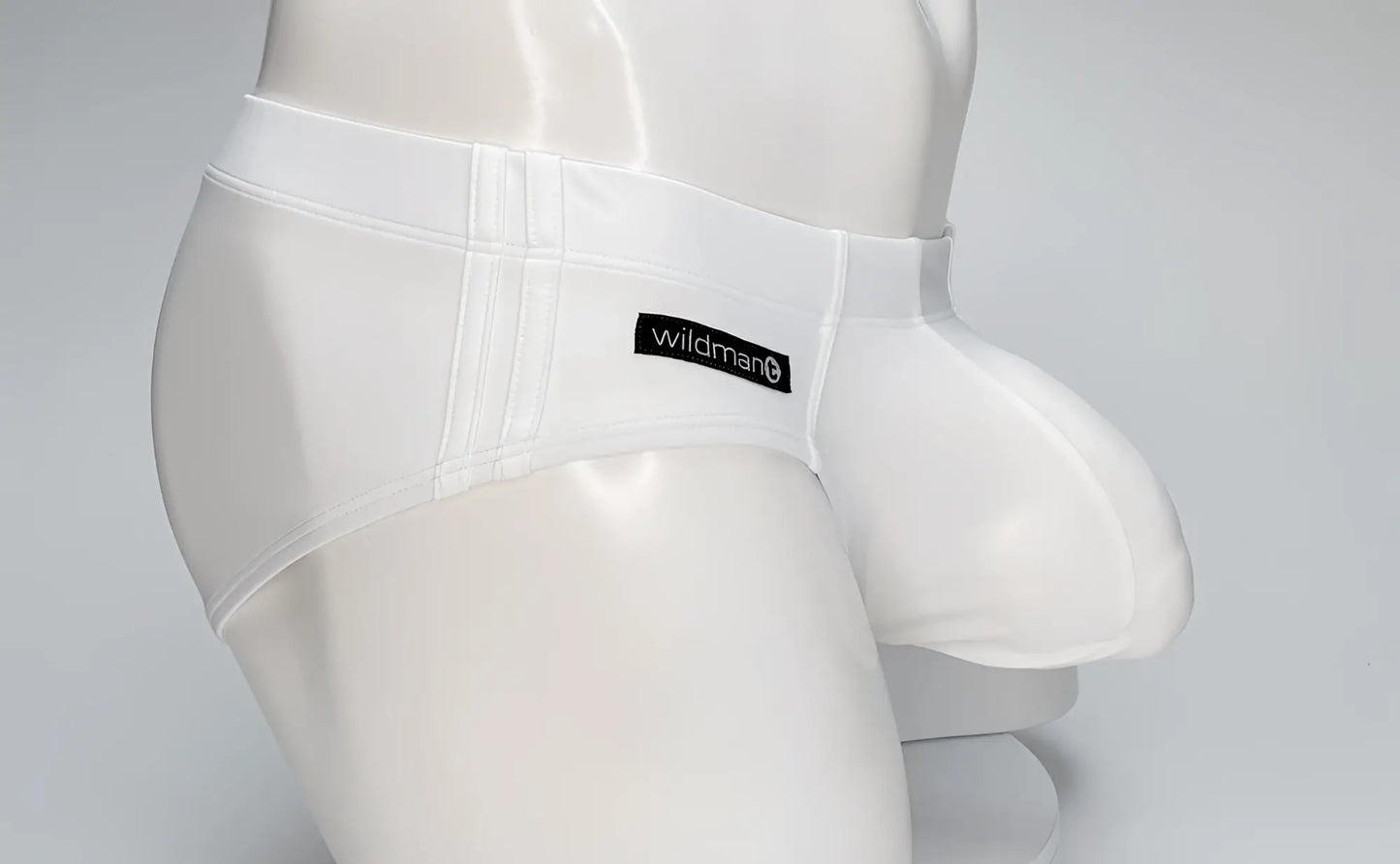 White WildmanT swim brief with a large front pouch and black branded tag, worn by a white mannequin torso.