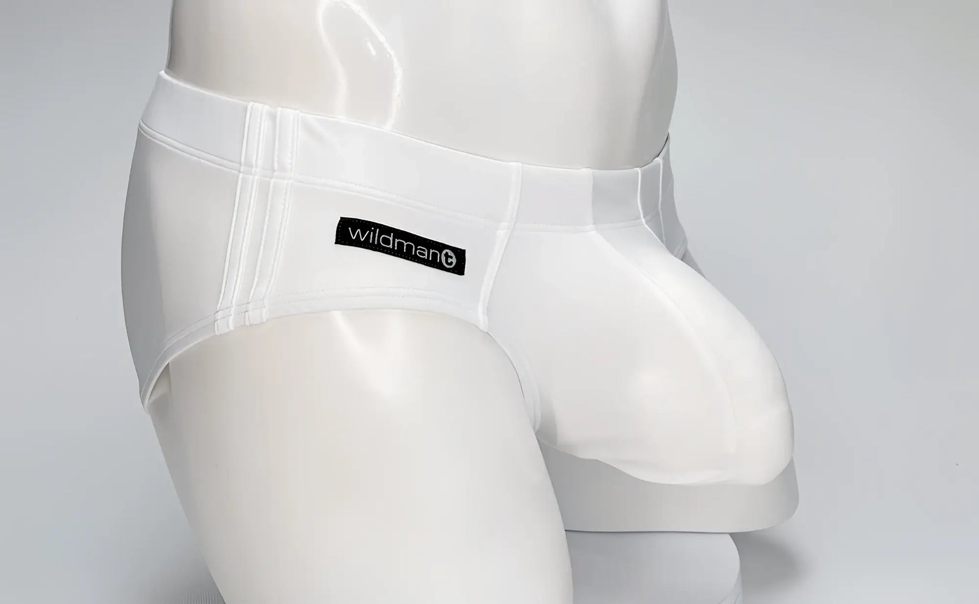 White WildmanT swim brief on a mannequin, featuring a contoured, prominent pouch and a black logo tab on the hip.