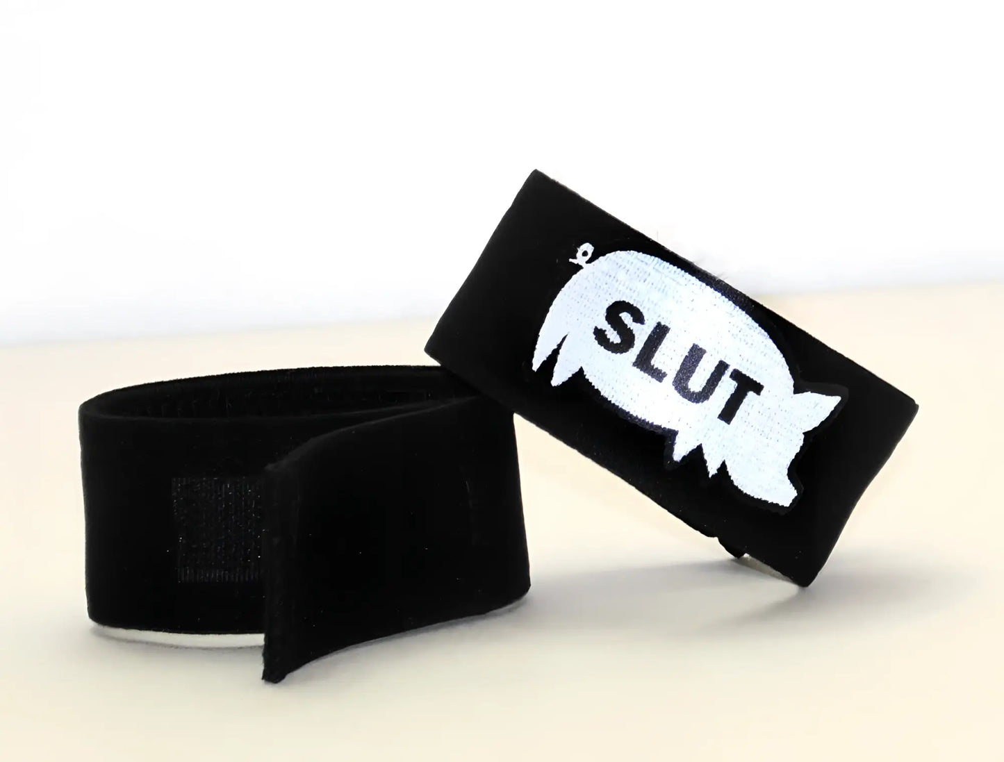 Black velour wristband with white embroidered speech bubble and slut text from wildmant fetish max cock-ring-pig slut product