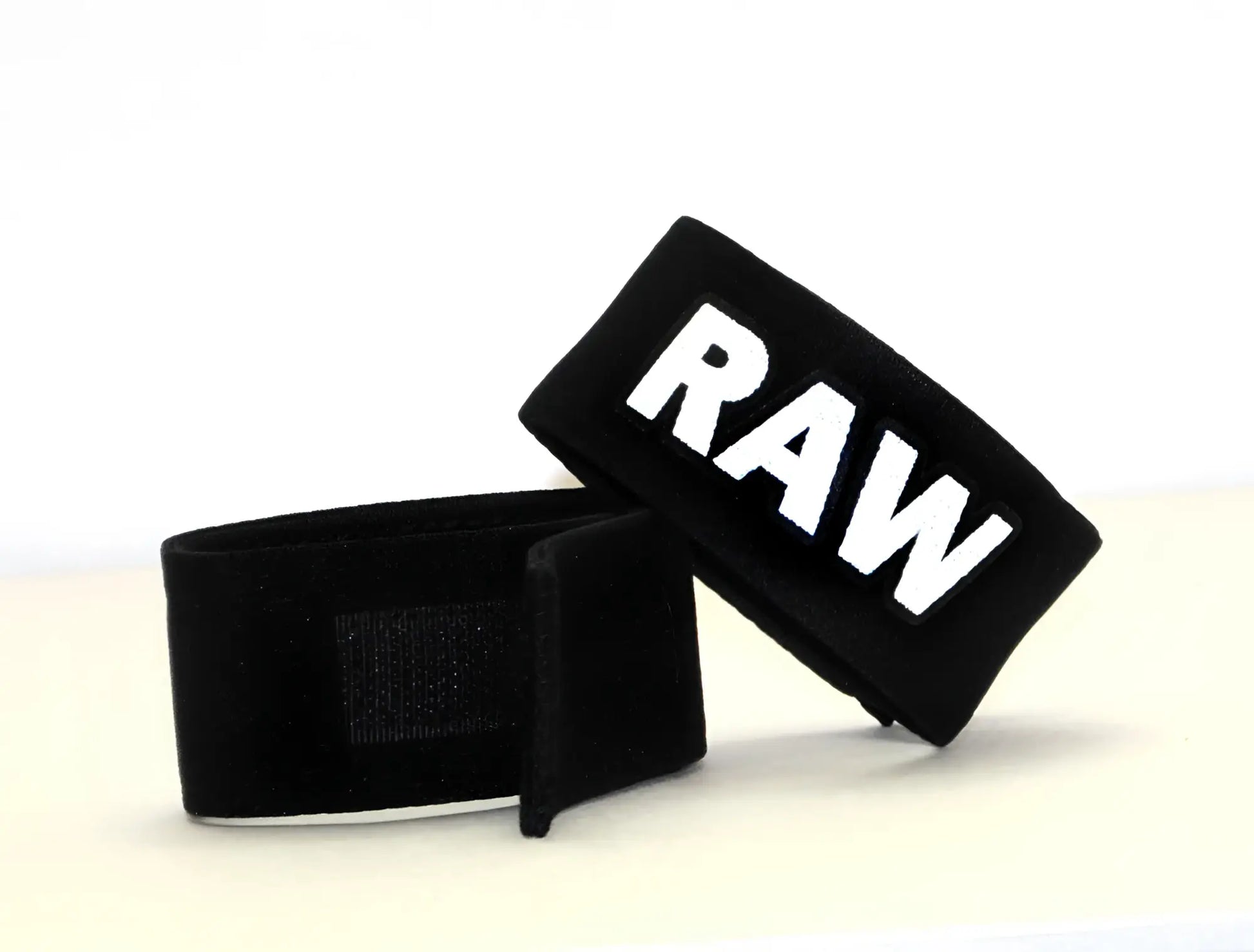 Black fabric wrist wraps with bold white raw lettering for wildmanT fetish max cock ring raw product use