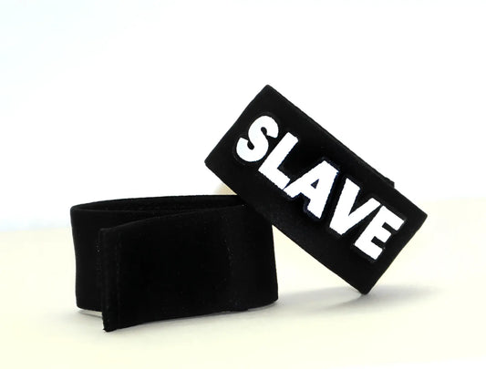 Black fabric cock ring with a "SLAVE" patch in bold white lettering, featuring a hook-and-loop closure.