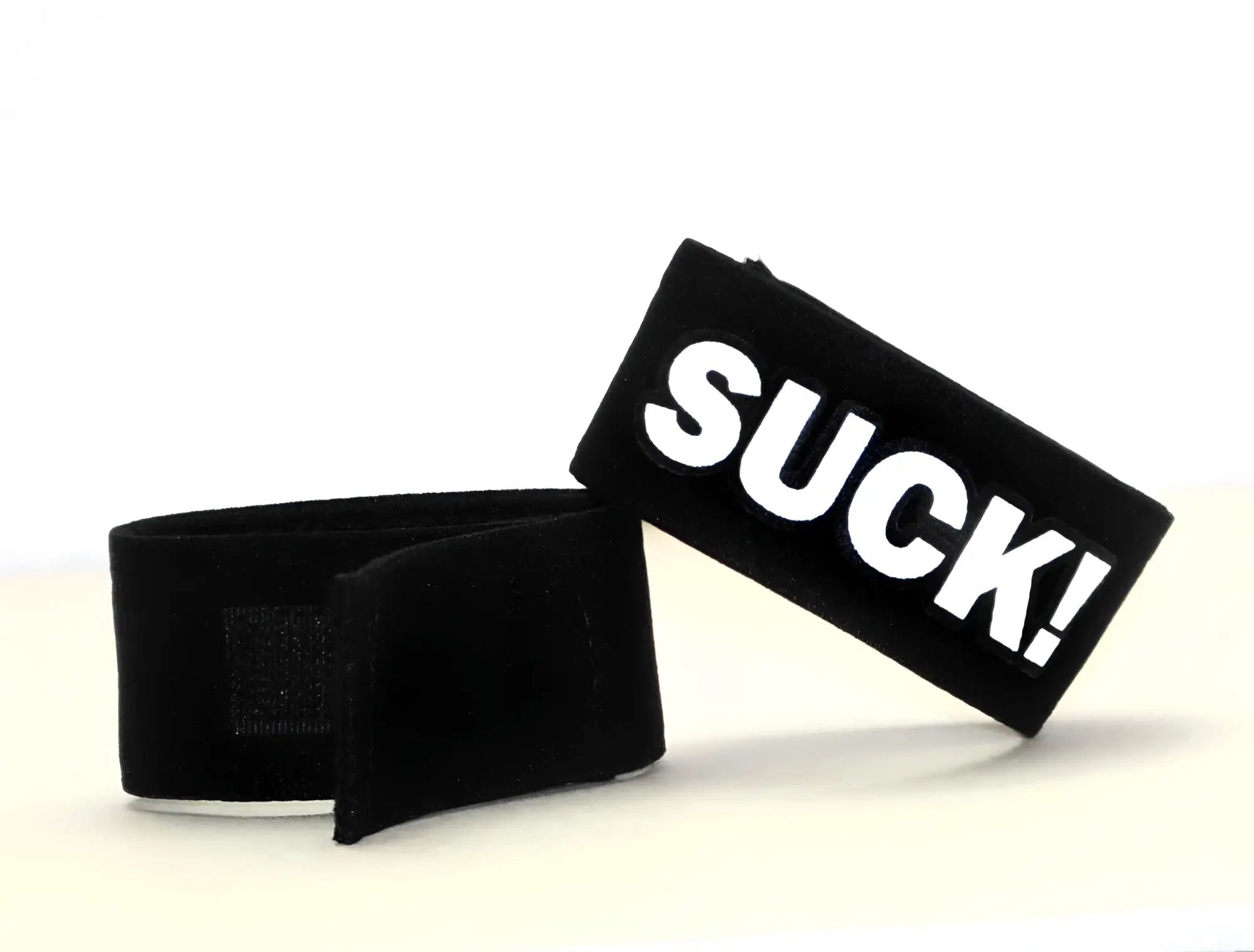 Black velour wristband with bold white suck lettering from wildmant fetish max cock ring suck collection