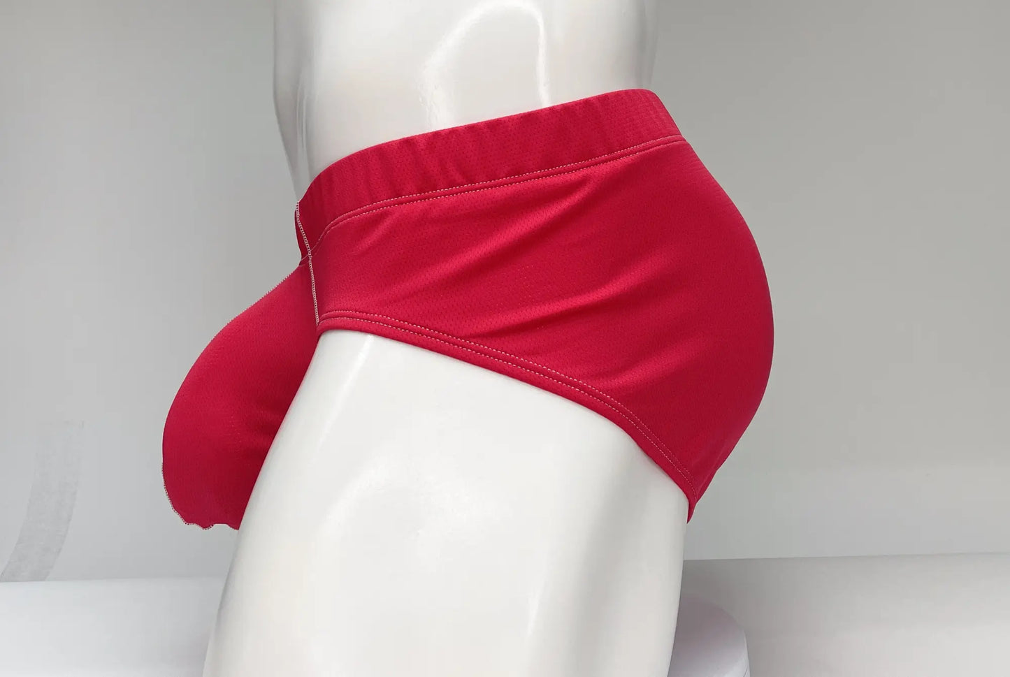 WildmanT mesh brief red showing smooth fabric red form-fitting swim trunks with visible stitching on the waistband