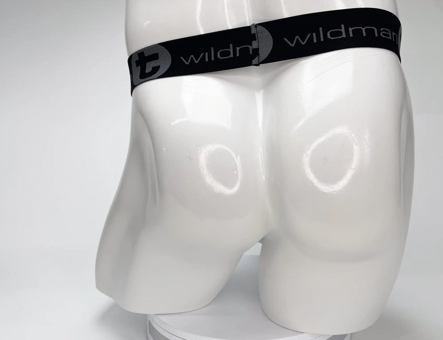 Black elastic waistband with wildman branding and stylized t logo on white mannequin of wildmant mesh monster cock strapless pouch