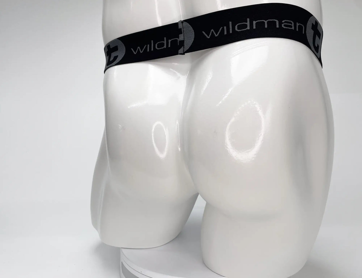 White strapless jockstrap on a mannequin, featuring a black branded elastic waistband with grey "WildmanT" logo text.