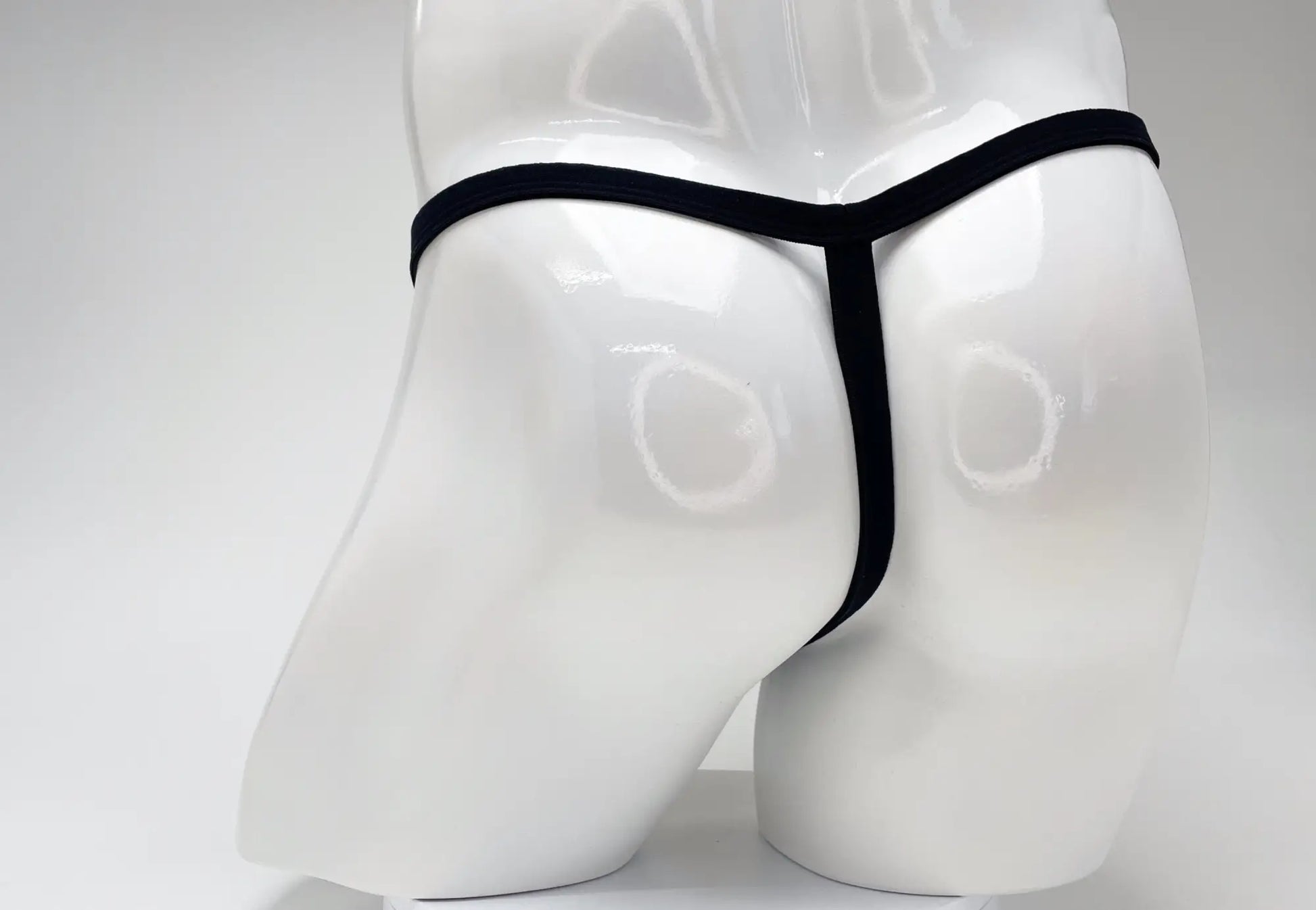 Back view of a black modal micro thong on a glossy white male mannequin torso.
