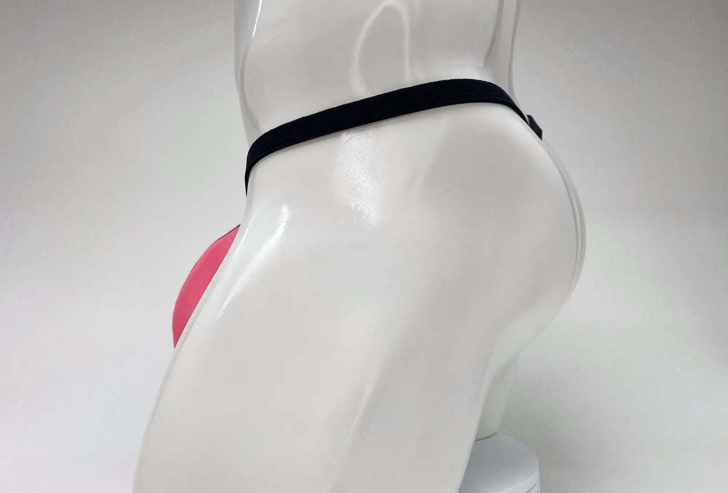Side view of a bright pink modal micro thong on a white mannequin, featuring a contoured pouch and black waistband.