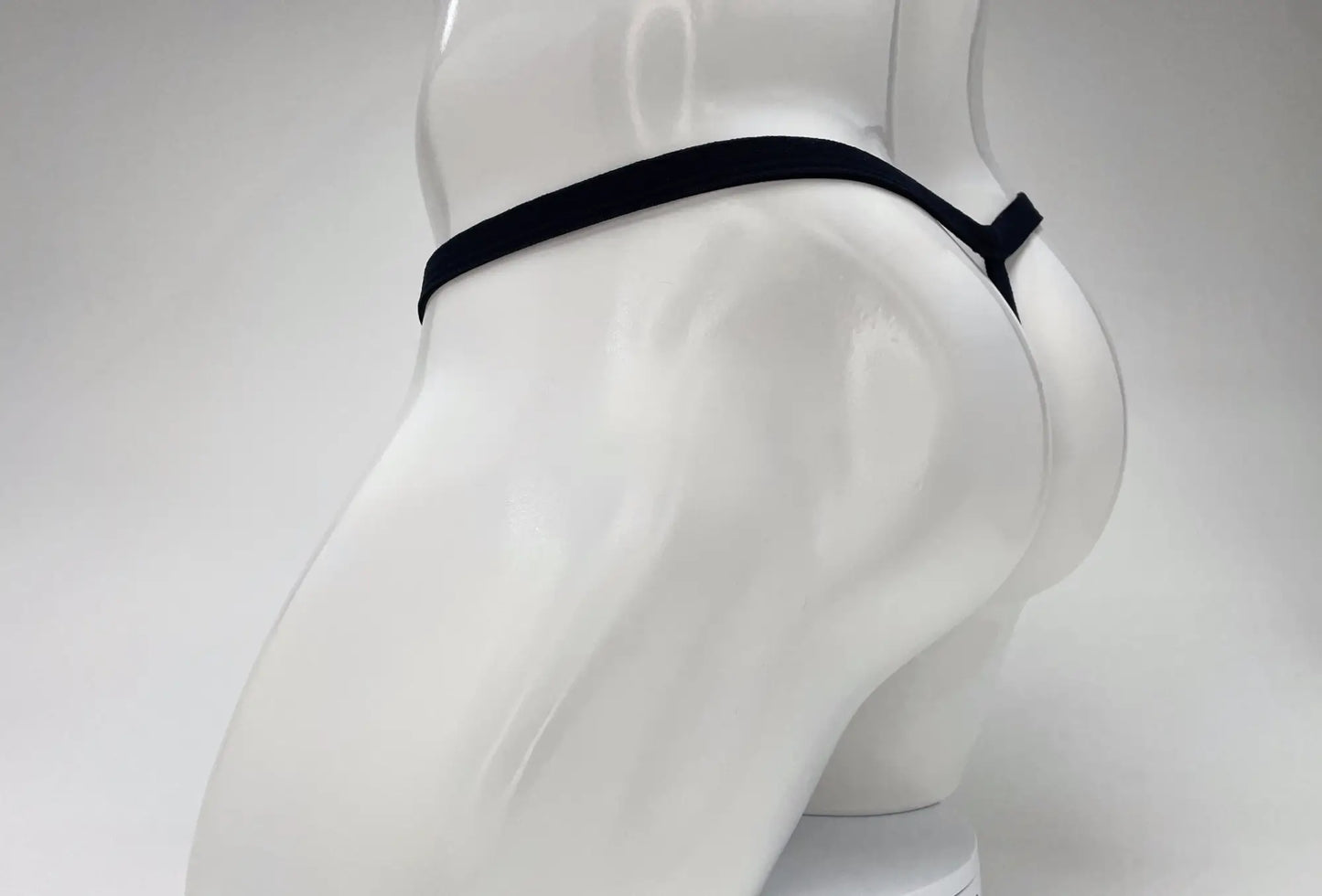 Black micro thong on a white mannequin, showing a minimalist string design from a side-rear perspective.