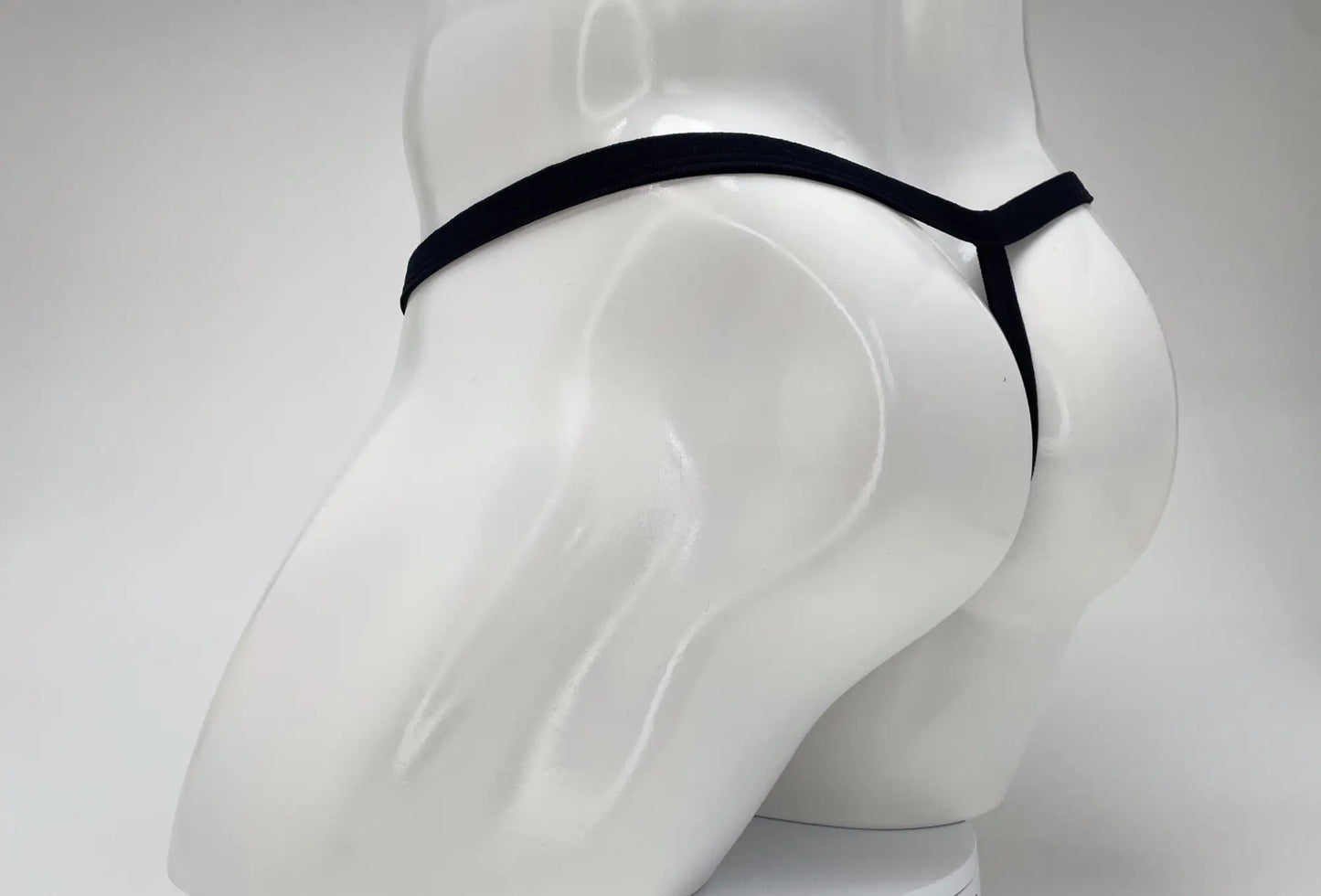 A black WildmanT micro thong with thin straps shown from behind on a white mannequin torso.