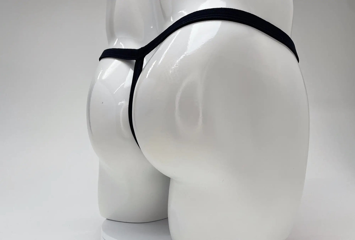 Rear view of a white mannequin wearing a thin, black modal micro thong with a minimalist strap design.