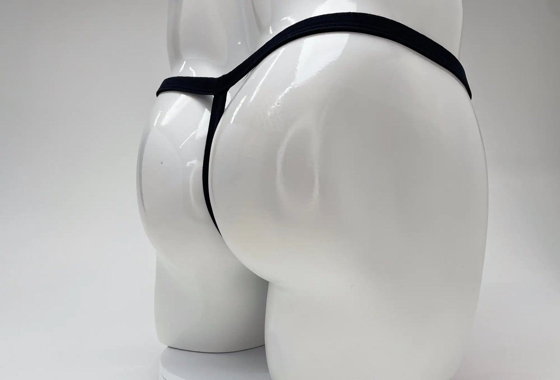 Rear view of a white mannequin wearing a thin, black modal micro thong with a minimalist strap design.