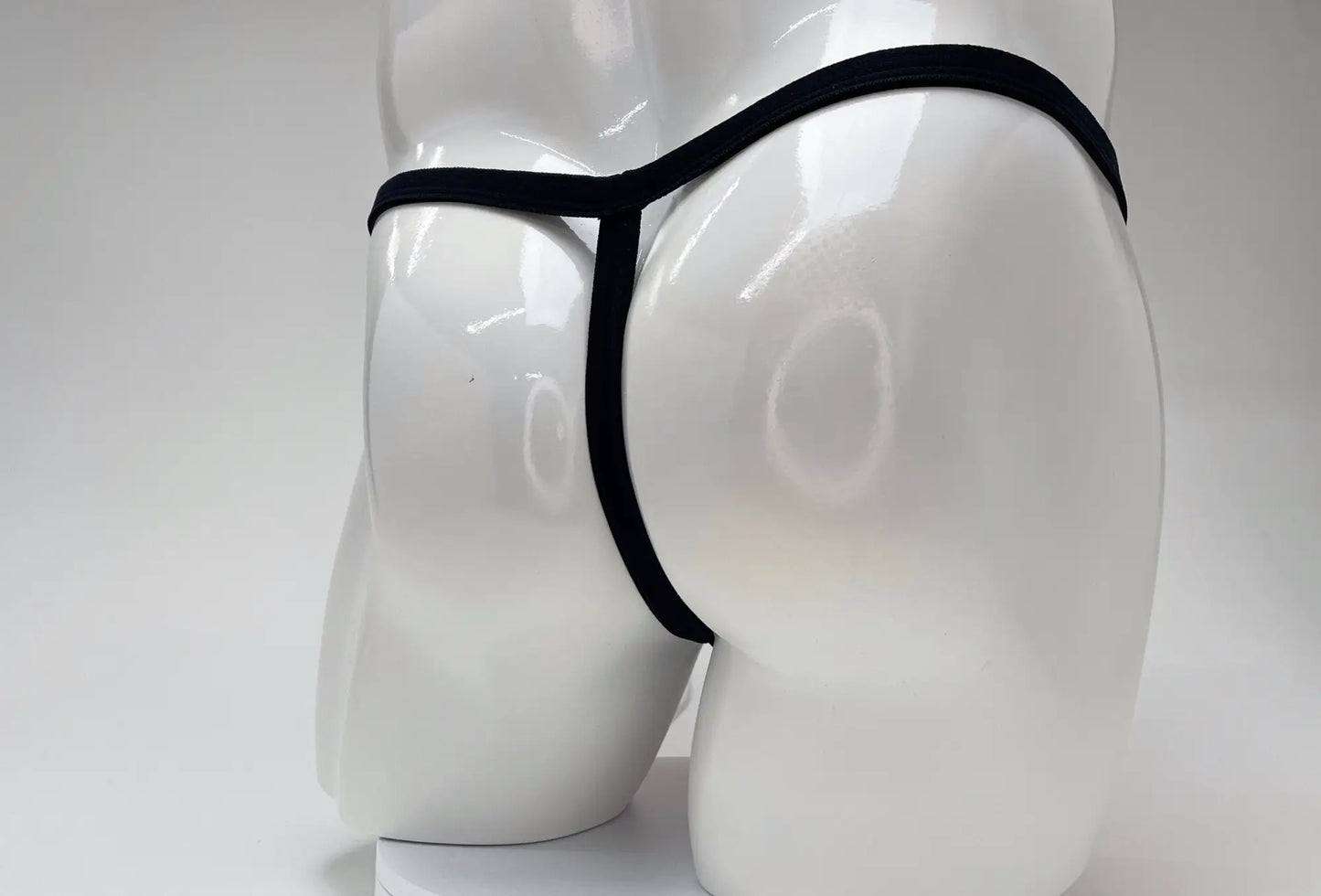 Rear view of a black micro thong on a white mannequin torso, highlighting the minimalist string design.
