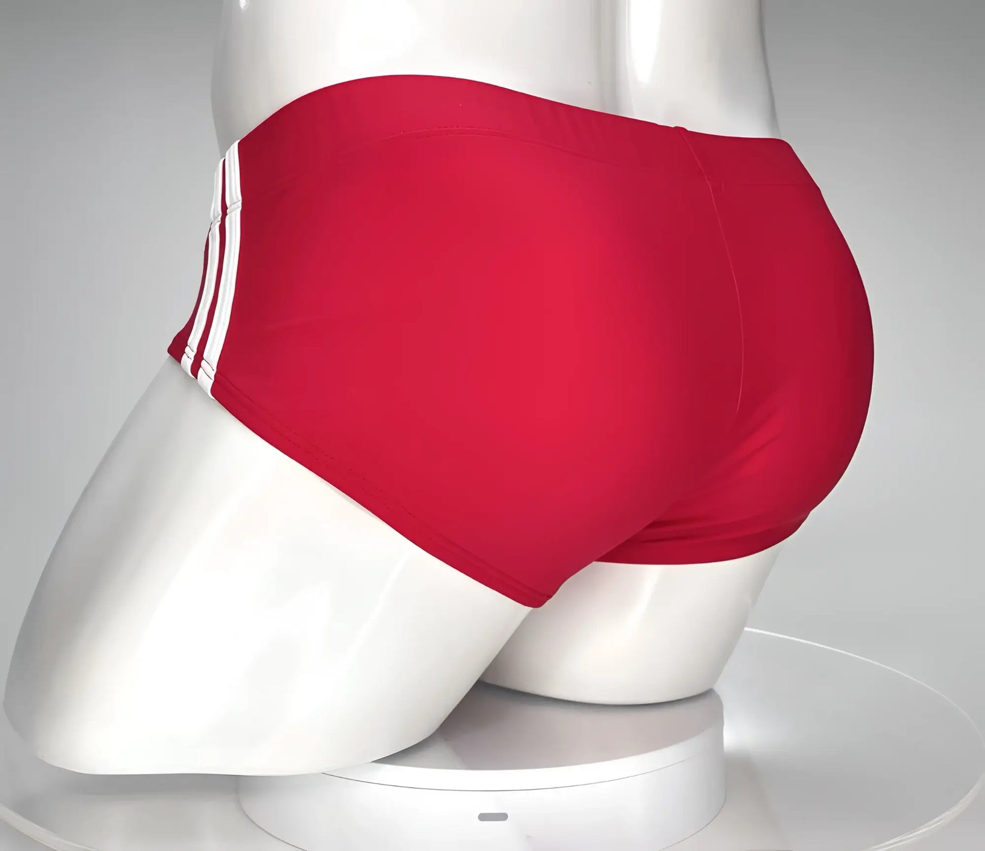 WildmanT monster cock swim brief red featuring red swim trunks with three white stripes on the side displayed on a mannequin