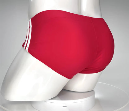 WildmanT monster cock swim brief red featuring red swim trunks with three white stripes on the side displayed on a mannequin