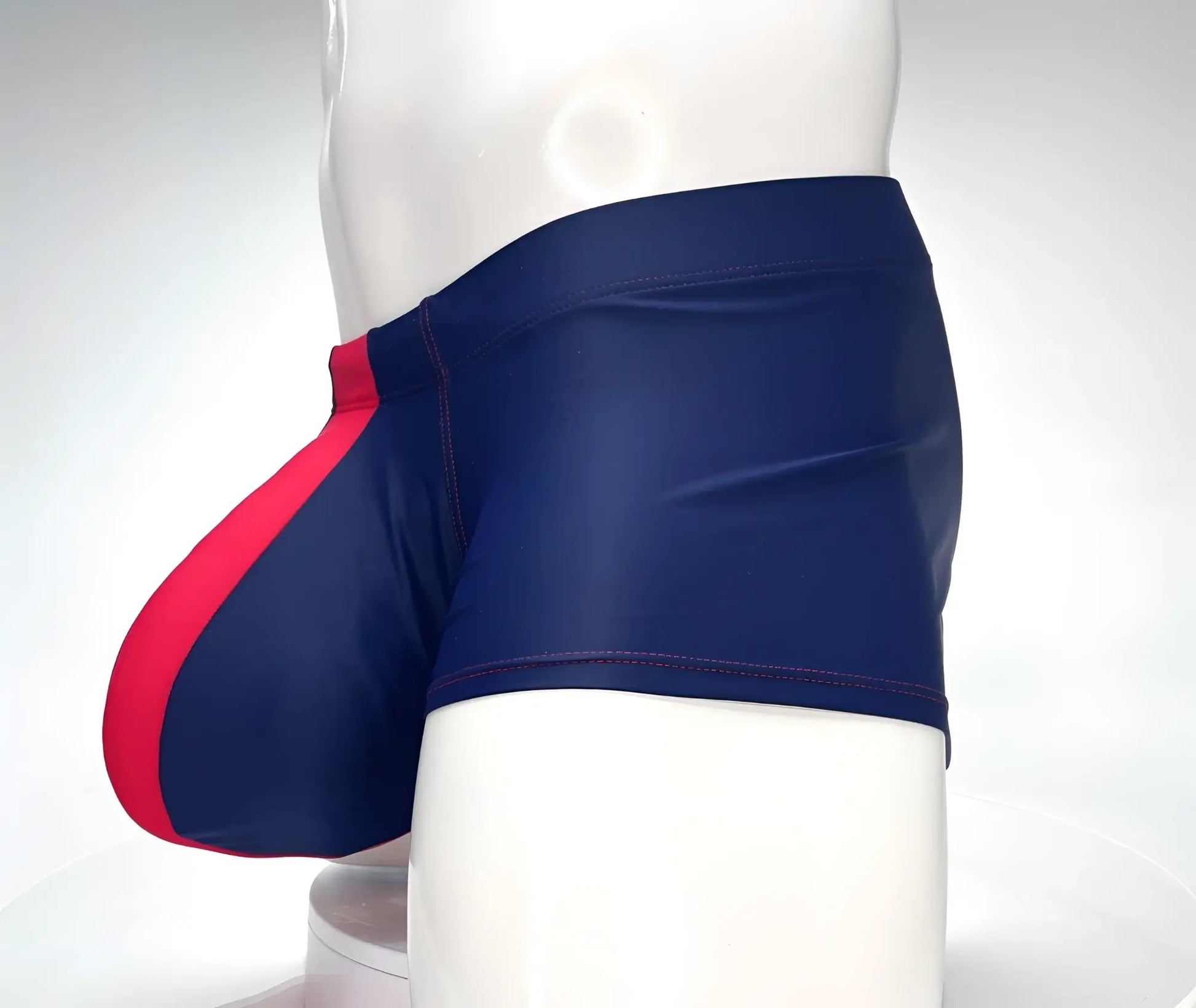 Navy blue square-cut swim trunks with a bright red front pouch and red contrast stitching on a mannequin.