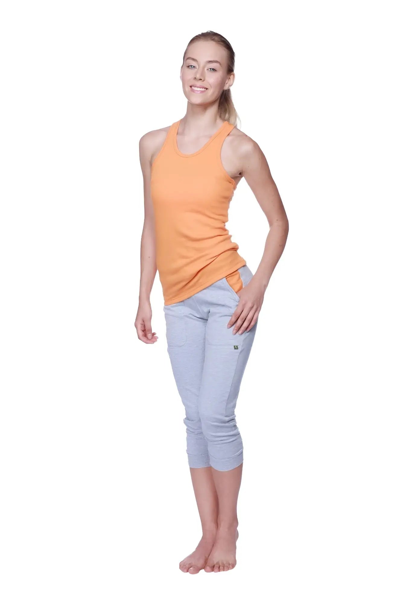 A woman wearing a soft sun orange women’s all-american racerback tank top with light gray capri pants facing forward