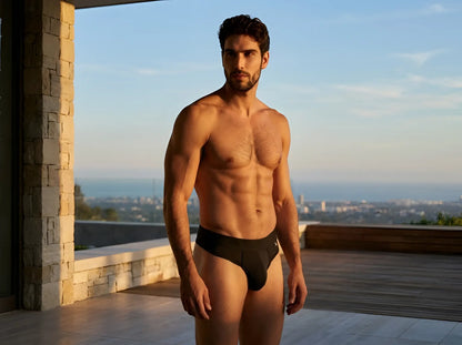 Xtremen black thong worn by a shirtless man on a balcony, featuring a minimalist design and fitted waistband.