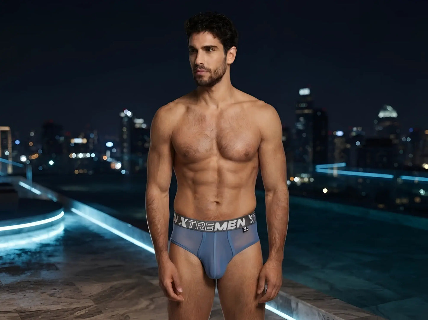 Xtremen blue bikini brief in sheer mesh fabric with a branded elastic waistband on a model at night.