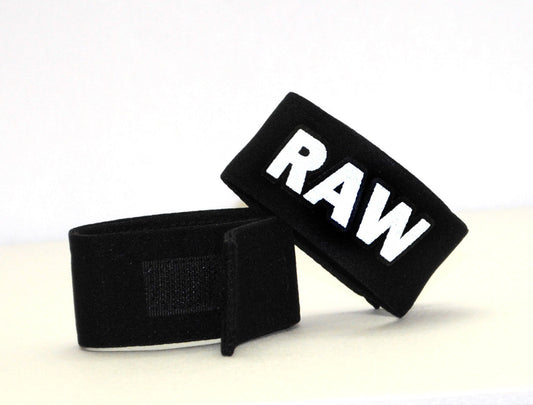 Black fabric wrist wraps with bold white raw lettering for wildmanT fetish max cock ring raw product use